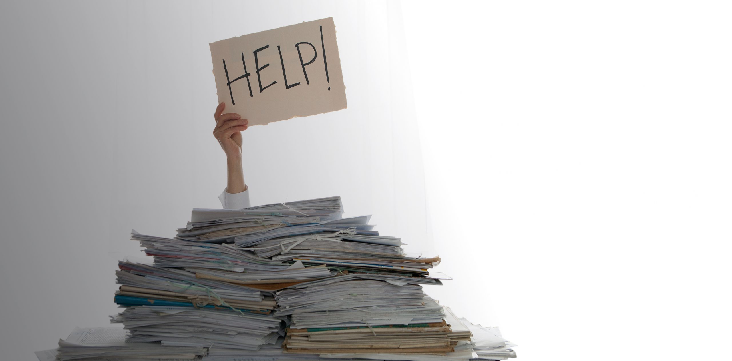 Person under a pile of papers with a hand holding a sign of help. Accounting.