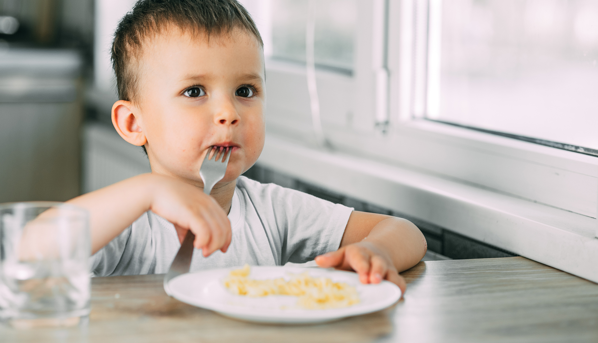 a little boy eats pasta in the form of a spiral in the afternoon in the kitchen on their own very appetizing